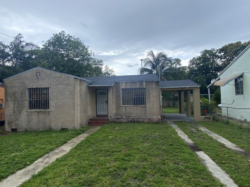 An Allapattah house before renovation, bare block walls and a worn driveway