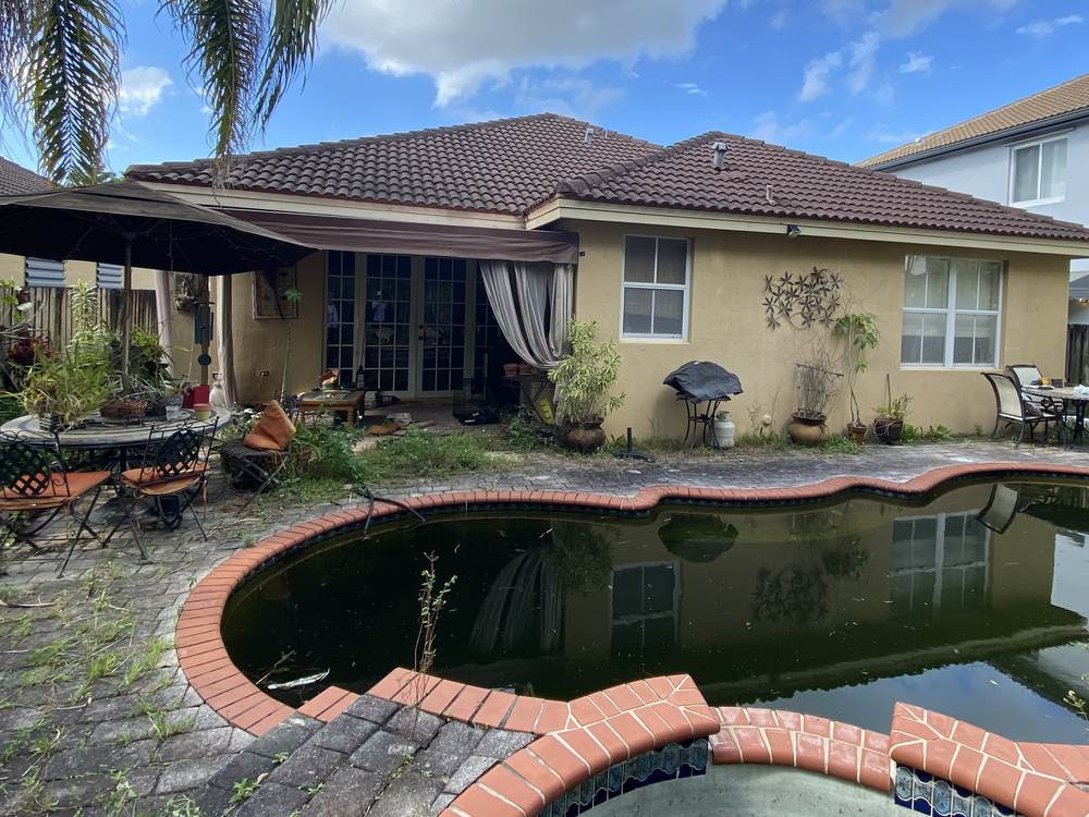 A Kendall house before renovation, with a stagnant green pool and an overgrown patio