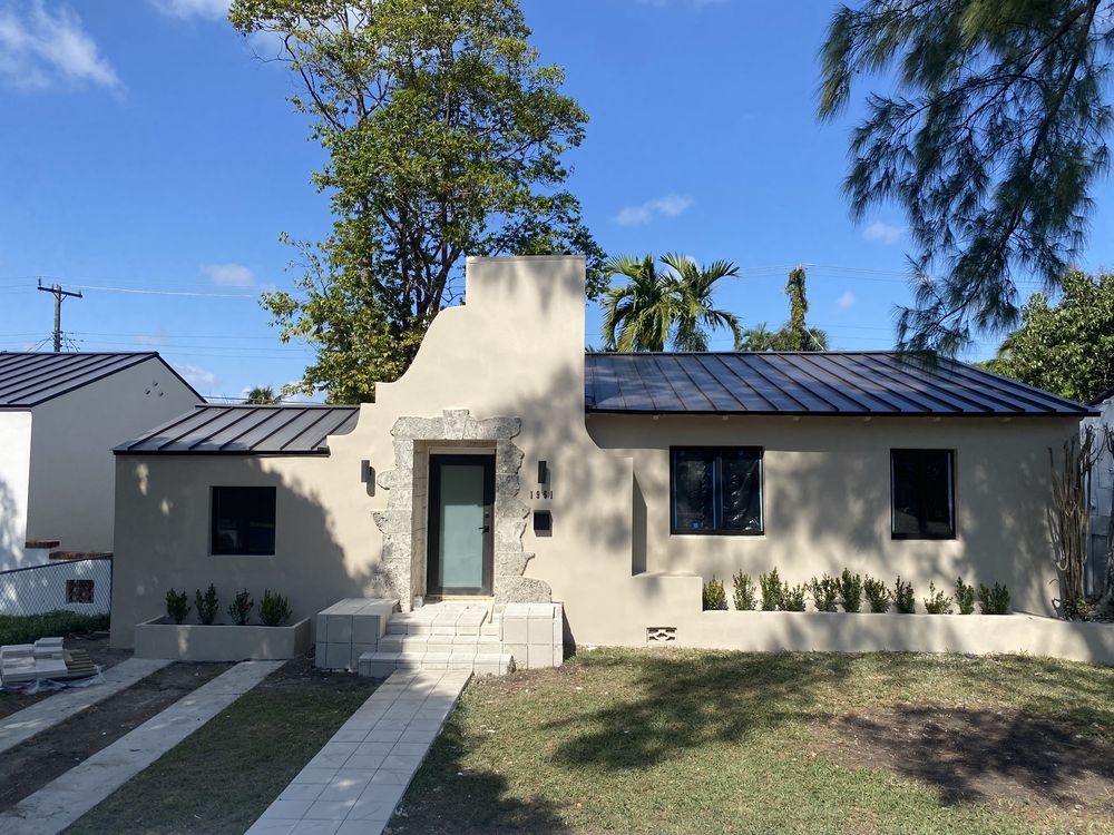 The same house after a full gut renovation, with a new standing-seam metal roof, new stucco, and the coral rock kept